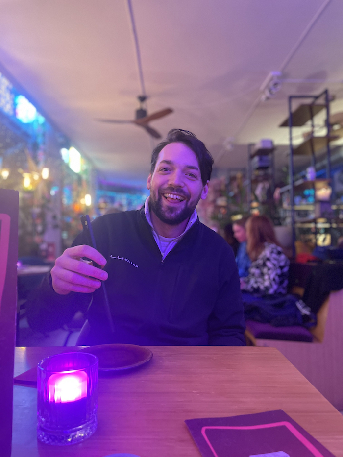 A man handles chopsticks at a restaurant, a warm neon background