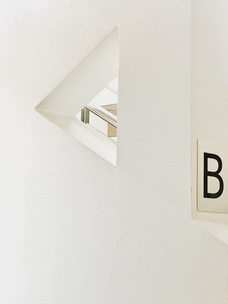 Angled hole in a white wall makes for an abstract view, letter B displayed on the side